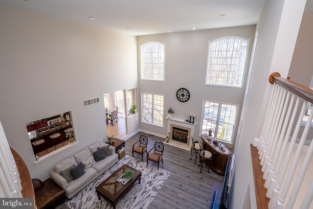 living area featuring recessed lighting, wood finished floors, a towering ceiling, a fireplace with flush hearth, and visible vents