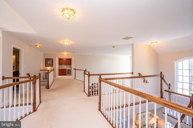 hall featuring light carpet, visible vents, and an upstairs landing