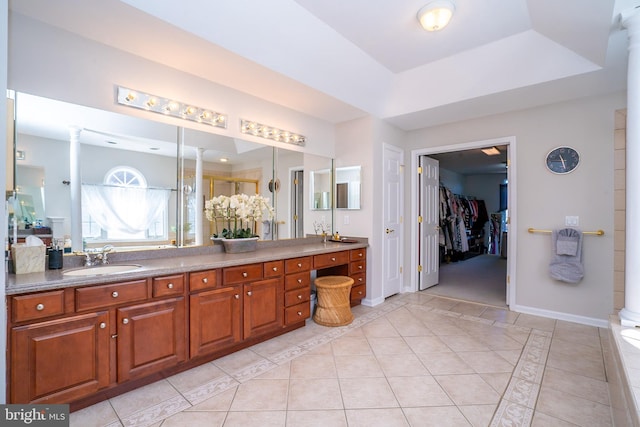 bathroom with decorative columns, a tray ceiling, a sink, and tile patterned floors