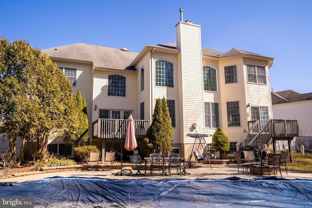 rear view of property featuring a deck, a patio, a chimney, and stairs