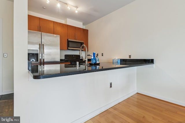 kitchen with light wood finished floors, baseboards, brown cabinetry, dark countertops, and stainless steel appliances