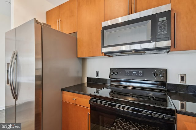 kitchen with stainless steel appliances, brown cabinetry, and dark stone countertops