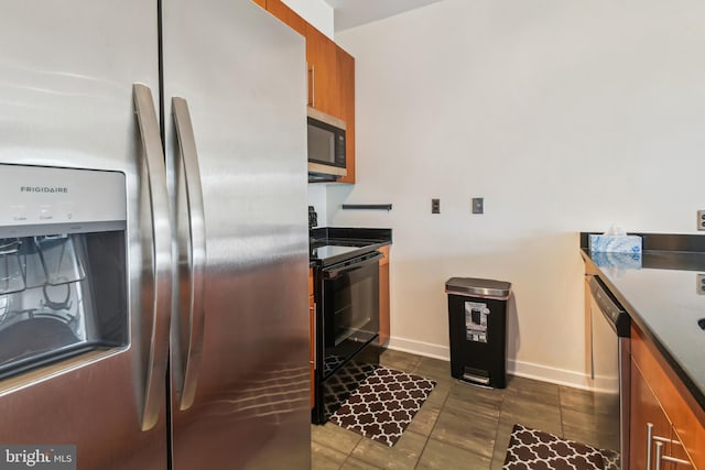 kitchen with stainless steel appliances, dark countertops, brown cabinetry, and baseboards