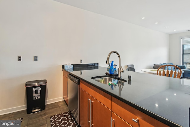 kitchen featuring baseboards, brown cabinetry, dark countertops, stainless steel dishwasher, and a sink