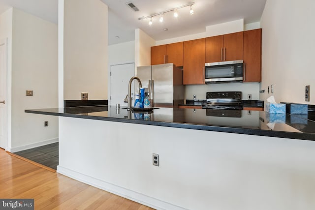 kitchen featuring dark countertops, appliances with stainless steel finishes, wood finished floors, a peninsula, and a sink