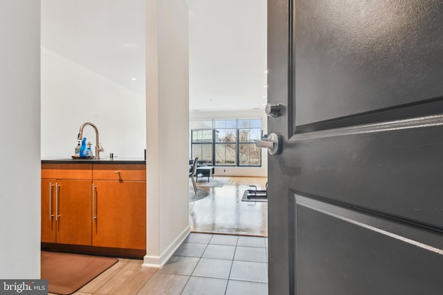 interior space with light tile patterned floors, brown cabinetry, a sink, and baseboards