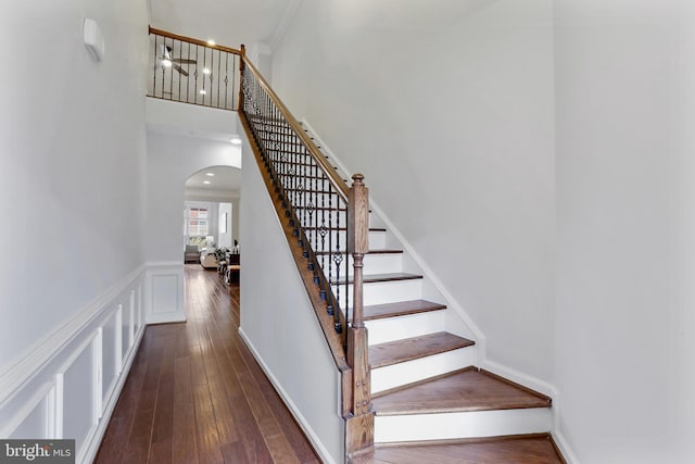 stairway with arched walkways, a high ceiling, wood finished floors, and a decorative wall