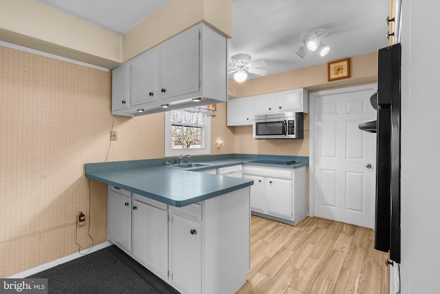 kitchen with black appliances, light countertops, white cabinetry, and wallpapered walls