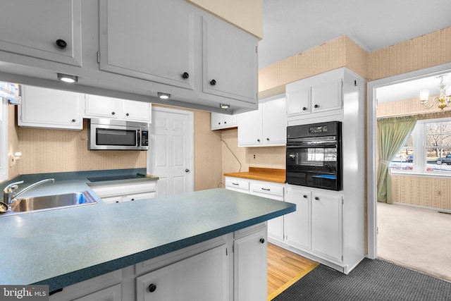 kitchen featuring stainless steel microwave, white cabinetry, a sink, black oven, and wallpapered walls