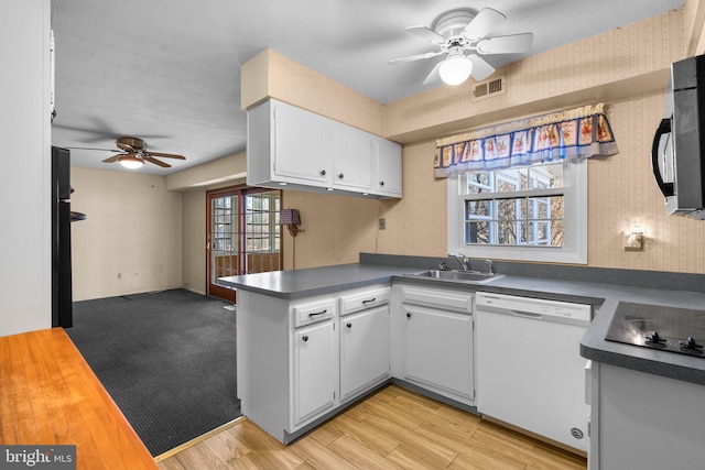 kitchen with wallpapered walls, visible vents, dark countertops, white dishwasher, and a sink