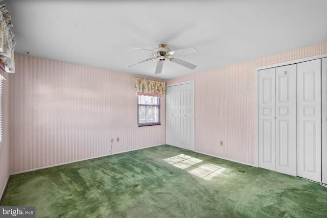 unfurnished bedroom with multiple closets, dark colored carpet, a ceiling fan, and wallpapered walls