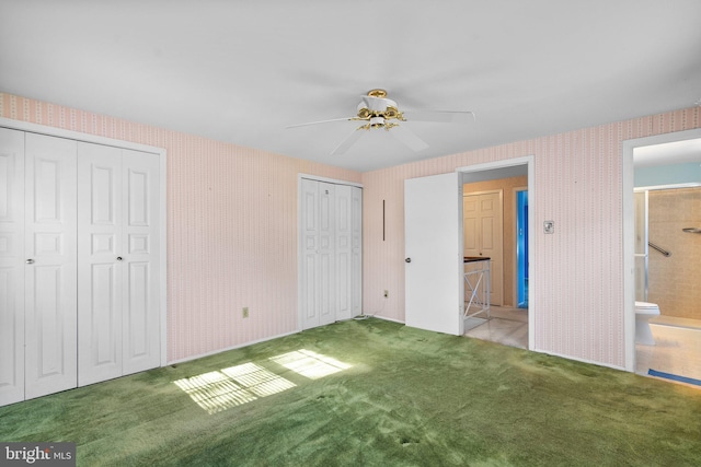 unfurnished bedroom with multiple closets, light colored carpet, a ceiling fan, ensuite bath, and wallpapered walls