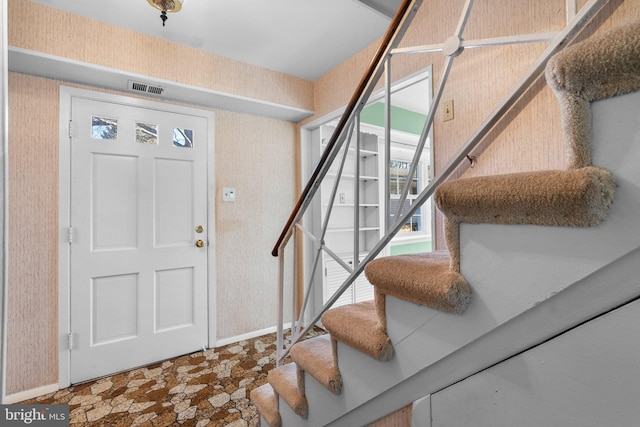 foyer entrance featuring wallpapered walls, stone finish flooring, stairs, and visible vents