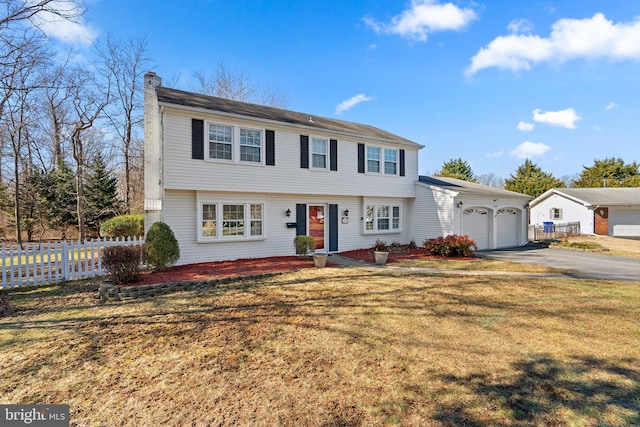 colonial home with a chimney, an attached garage, fence, driveway, and a front lawn