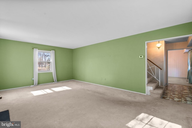 empty room with light colored carpet, baseboards, and stairs