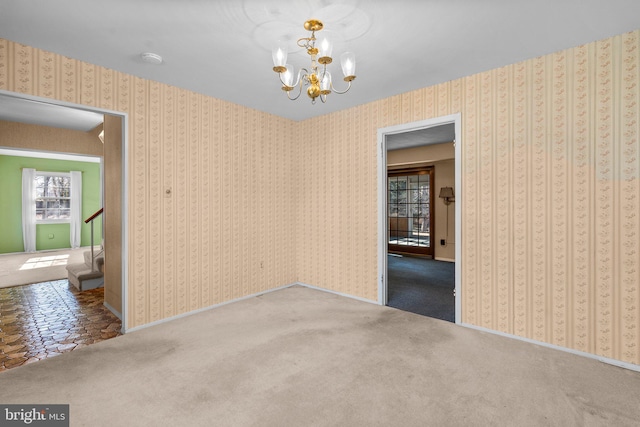 carpeted empty room featuring a notable chandelier, baseboards, and wallpapered walls