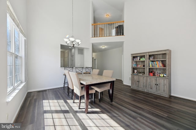 dining space with a notable chandelier, a towering ceiling, and wood finished floors