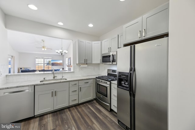 kitchen with stainless steel appliances, dark wood-type flooring, a sink, decorative backsplash, and light stone countertops