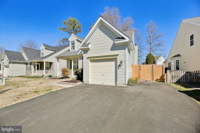 cape cod home with a garage, driveway, fence, and a porch