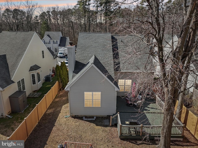 back of property at dusk featuring a fenced backyard, roof with shingles, central AC, and a wooden deck