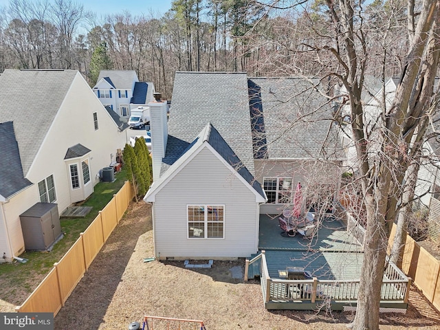 exterior space featuring a fenced backyard, a deck, central AC, and roof with shingles