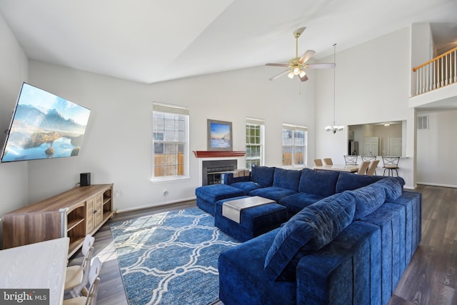 living room featuring baseboards, visible vents, a glass covered fireplace, wood finished floors, and ceiling fan with notable chandelier