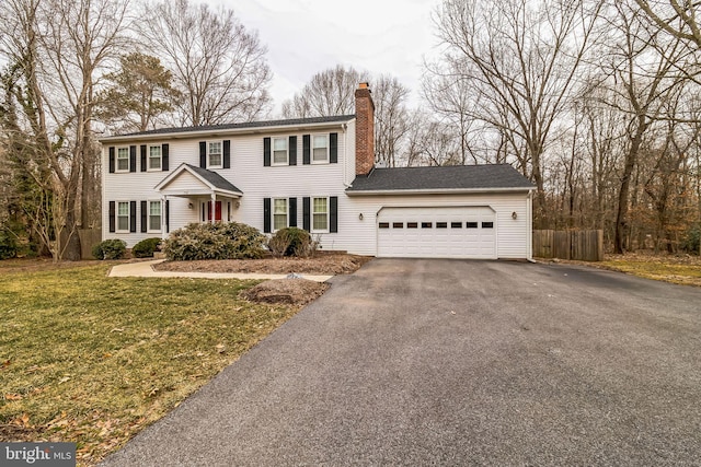 colonial inspired home featuring a chimney, fence, a garage, driveway, and a front lawn