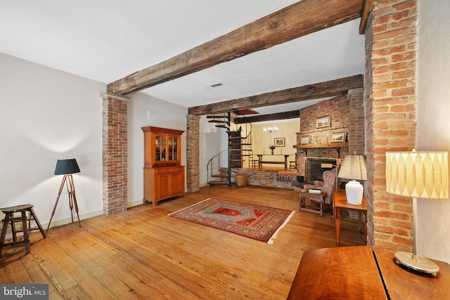 living room featuring baseboards, wood-type flooring, stairway, beamed ceiling, and a fireplace