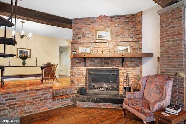 living area featuring beam ceiling, a brick fireplace, hardwood / wood-style flooring, and an inviting chandelier