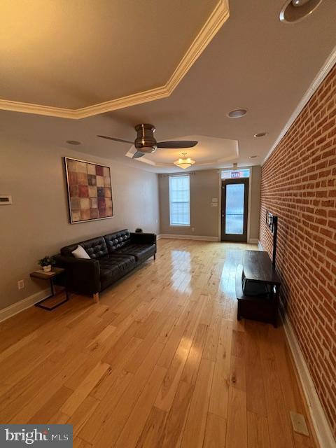 unfurnished living room with ornamental molding, ceiling fan, brick wall, wood finished floors, and baseboards