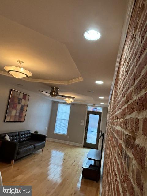 living area featuring a tray ceiling, recessed lighting, light wood-style flooring, ornamental molding, and baseboards