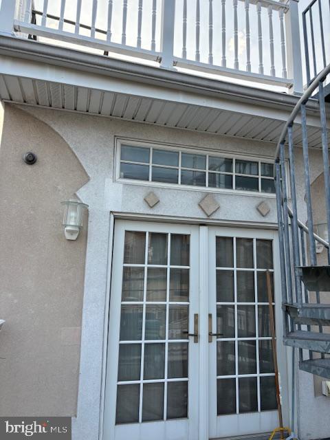 view of exterior entry featuring french doors, a balcony, and stucco siding