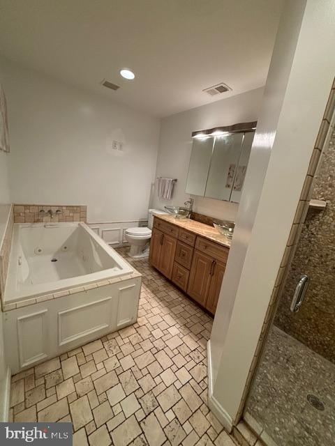 bathroom with toilet, double vanity, a jetted tub, and visible vents