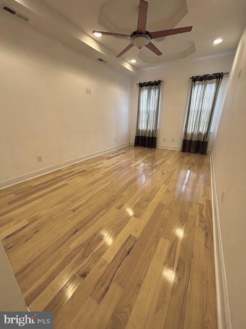 empty room with light wood-style flooring, recessed lighting, visible vents, baseboards, and a raised ceiling