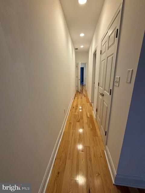 hall featuring light wood-style flooring, baseboards, and recessed lighting