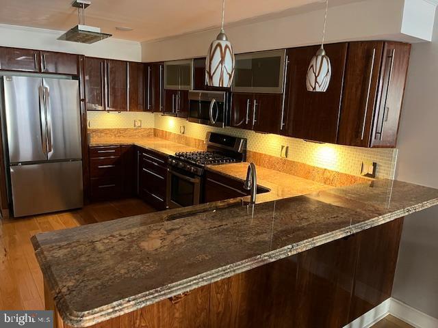 kitchen featuring appliances with stainless steel finishes, hanging light fixtures, a peninsula, and dark brown cabinetry