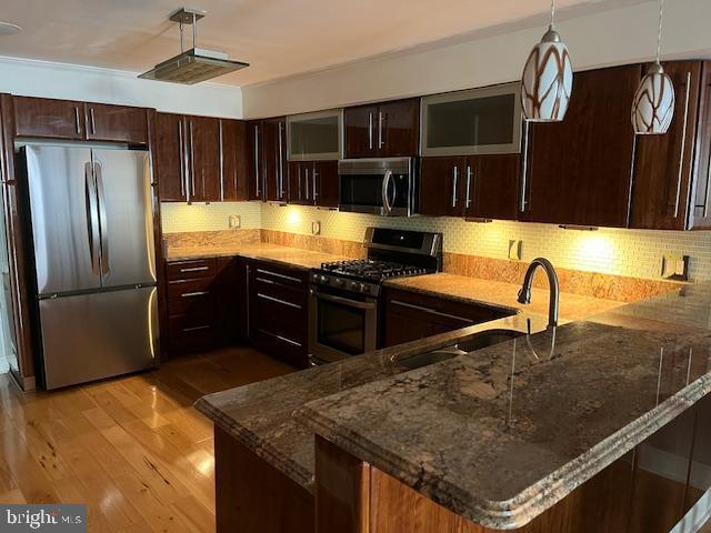 kitchen featuring dark stone counters, appliances with stainless steel finishes, hanging light fixtures, a peninsula, and dark brown cabinets