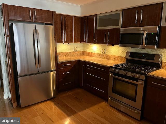 kitchen featuring appliances with stainless steel finishes, light wood-style floors, light stone counters, and tasteful backsplash