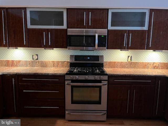 kitchen featuring dark brown cabinetry, light stone countertops, stainless steel appliances, and decorative backsplash