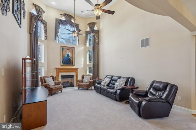 carpeted living room featuring a fireplace, visible vents, a high ceiling, a ceiling fan, and baseboards