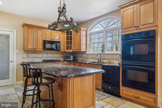 kitchen featuring glass insert cabinets, a sink, a kitchen island, dark stone countertops, and black appliances