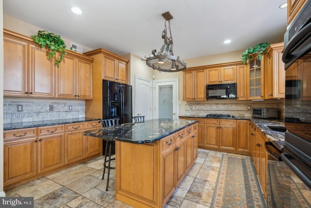 kitchen featuring glass insert cabinets, a kitchen island, hanging light fixtures, black appliances, and stone tile flooring