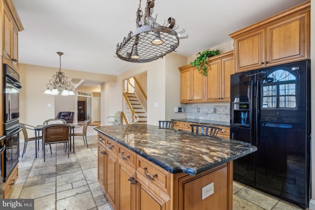 kitchen with hanging light fixtures, black appliances, stone tile floors, and a center island