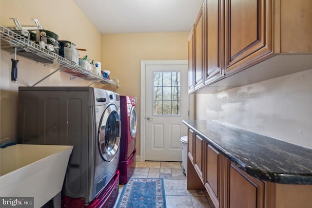 laundry area featuring washing machine and dryer, cabinet space, a sink, and stone tile flooring