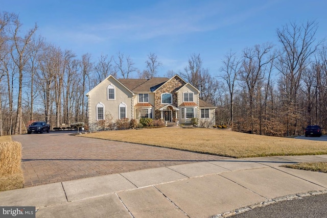 view of front facade with stone siding, a front yard, decorative driveway, and stucco siding