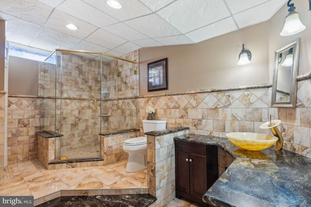 bathroom with a stall shower, tile walls, toilet, and vanity