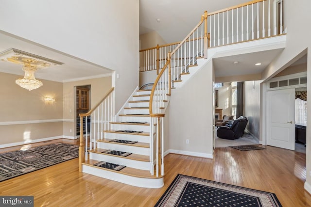 stairs featuring a notable chandelier, wood finished floors, a towering ceiling, and baseboards