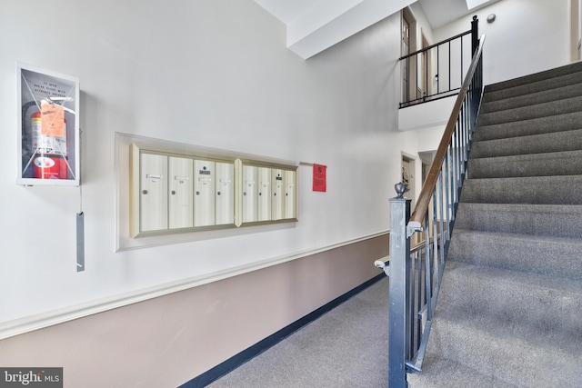 stairs featuring carpet floors, mail area, baseboards, and a towering ceiling