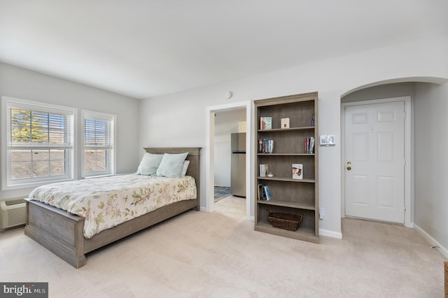 bedroom featuring light carpet, baseboards, arched walkways, freestanding refrigerator, and a wall mounted AC