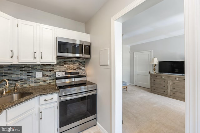 kitchen featuring decorative backsplash, appliances with stainless steel finishes, white cabinetry, a sink, and dark stone counters